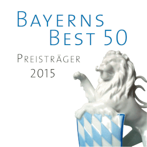 A white porcelain lion with a blue and white checkered shield in front of it. The text above it reads Bavaria's Best 50 Award Winners 2015 on a white background.